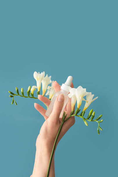 Hand holding fles met cosmetisch serum en bloemen op blauwe achtergrond - Foto, afbeelding