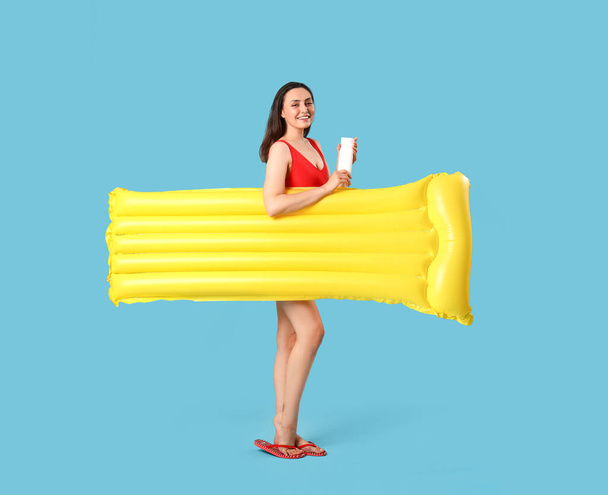 Young woman with sunscreen cream and inflatable mattress on blue background - Foto, afbeelding