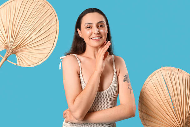 Young woman with sunscreen cream and fans on blue background - Foto, Bild