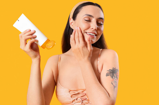 Young woman applying sunscreen cream on yellow background, closeup - Photo, Image