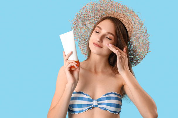 Young woman with sunscreen cream on blue background - Фото, зображення