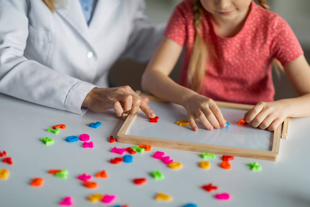 Μαθήματα Παιδικής Ανάπτυξης. Αγνώριστο μικρό κορίτσι που παίζει εκπαιδευτικά παιχνίδια κατά τη διάρκεια της ψυχολογικής διαβούλευσης, θηλυκό παιδί κάνει λέξεις από πολύχρωμα πλαστικά γράμματα, περικοπή shot - Φωτογραφία, εικόνα