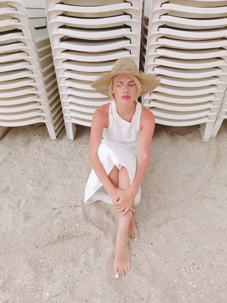 Portrait of fashion young woman wearing a straw hat. Sensual girl sitting on beach with copy space. Attractive girl looking at camera - Foto, imagen