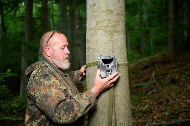 Hunter kamerát állít egy fára az erdőben. A nyomkövető kamerákat gyakran használják a vadászok automatikus fényképezés vagy videofelvétel vadon élő állatok az erdőben. - Fotó, kép