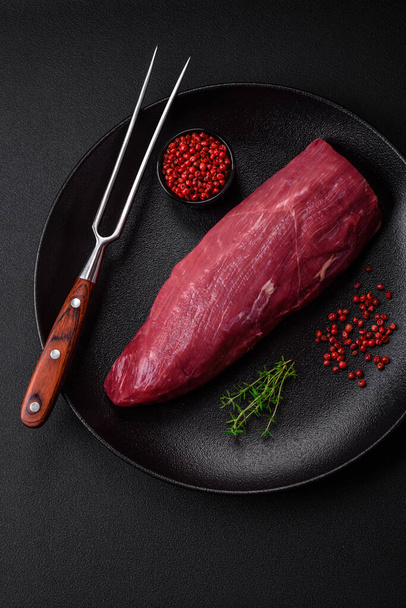 Saftiges rohes Rindfleisch mit Gewürzen, Salz und Kräutern auf dunklem Betongrund. Vorbereitung auf ein Fleischgericht - Foto, Bild