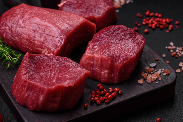 Saftiges rohes Rindfleisch mit Gewürzen, Salz und Kräutern auf dunklem Betongrund. Vorbereitung auf ein Fleischgericht - Foto, Bild