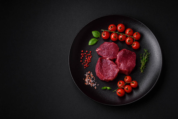 Ζουμερό ωμό βόειο κρέας με μπαχαρικά, αλάτι και βότανα σε σκούρο τσιμεντένιο φόντο. Προετοιμασία για το μαγείρεμα ενός πιάτου κρέατος - Φωτογραφία, εικόνα