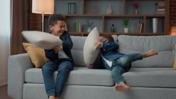 İki küçük yaramaz çocuk yastıklarla kavga ediyor Afrikalı Amerikalı kardeşler etnik çocuklar dövüş oyunu oynuyorlar oturma odasında kanepede oyun oynuyorlar hiperaktif davranış - Video, Çekim