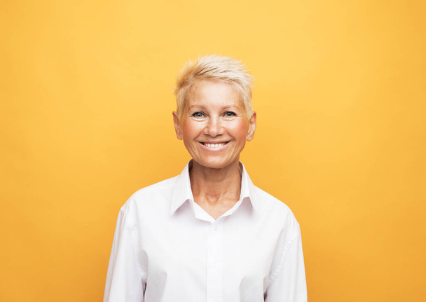Elderly beautiful woman with a short pixie haircut on a yellow color background. Close up portrait. - Foto, Bild
