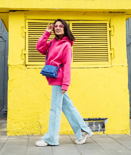 Beautiful stylish Asian young woman in pink sweatshirt and jeans posing while looking at the camera, lifestyle concept. - Fotoğraf, Görsel