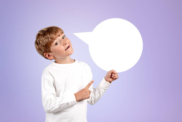Kid boy looking at the camera and fingers pointing to the side on purple background. Concept of idea and recommend. Speech bubble empty copy space - Φωτογραφία, εικόνα