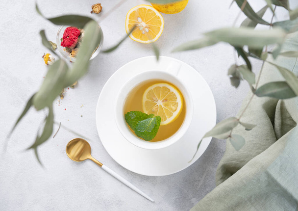 Tisane au citron et menthe dans une tasse blanche sur un fond clair avec des branches d'eucalyptus. Le concept d'une boisson saine et délicieuse pour l'immunité. Vue du dessus. - Photo, image