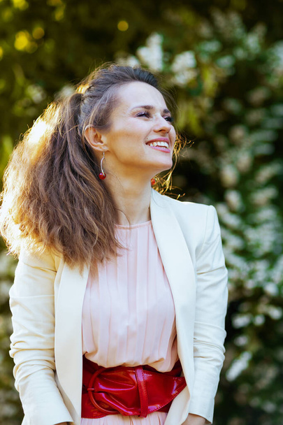 smiling elegant female in pink dress and white jacket in the city against greenery. - Fotografie, Obrázek
