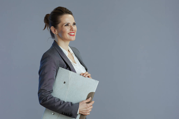smiling trendy 40 years old woman worker in grey suit with folder isolated on gray background. - 写真・画像
