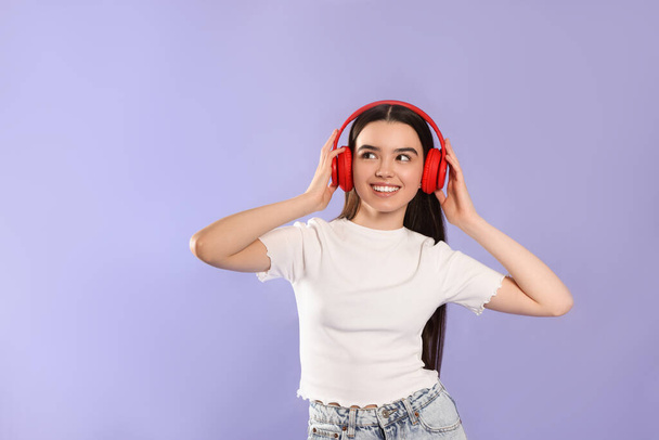 Teenage girl listening music with headphones on violet background - Foto, Imagem