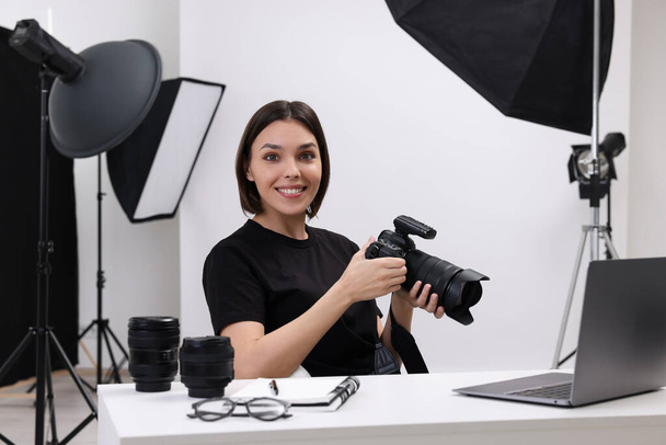 Young professional photographer with camera at table in modern photo studio - Foto, Imagen
