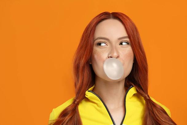 Portrait of beautiful woman blowing bubble gum on orange background. Space for text - 写真・画像