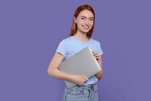 Smiling young woman with laptop on lilac background - 写真・画像