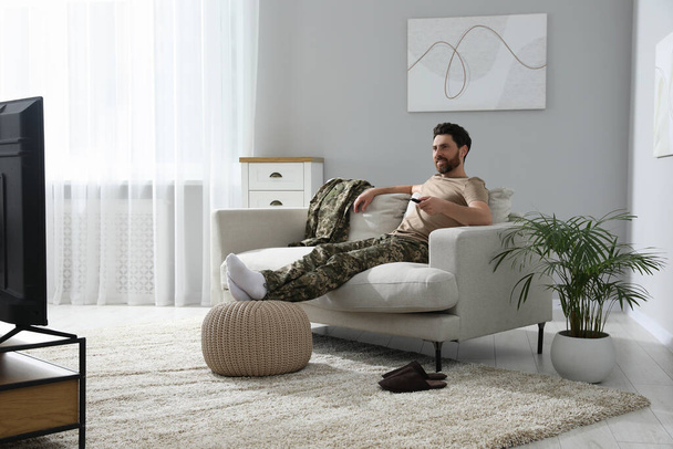 Happy soldier watching TV on sofa in living room. Military service - Photo, Image