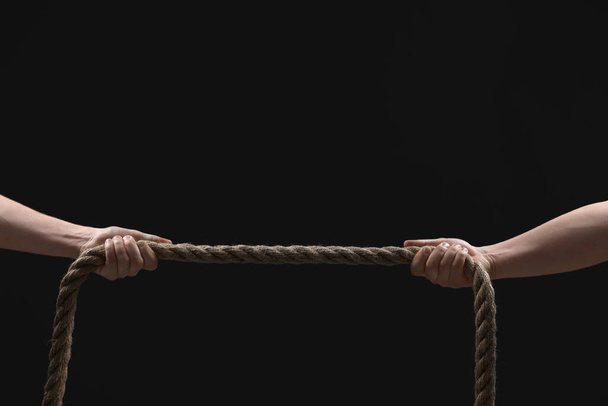 Dispute concept. Men pulling rope on black background, closeup. Space for text - Photo, image