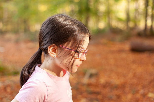 Dziewczynka w okularach na jesiennym tle lasu, widok z tyłu - Zdjęcie, obraz