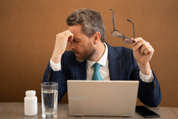 Millennial Businessman in office having headache. Business man in suit work on laptop at home office take off glasses suffer from migraine or headache. Tired exhausted man suffering from headache - Foto, Imagen