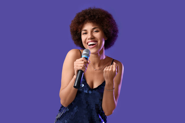 Curly young woman with microphone singing on purple background - Foto, Bild