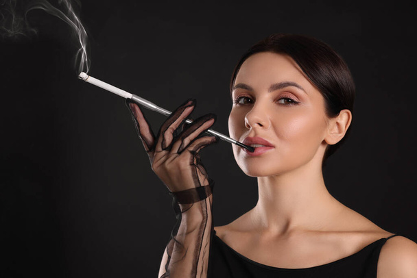 Woman using long cigarette holder for smoking on black background - Photo, Image