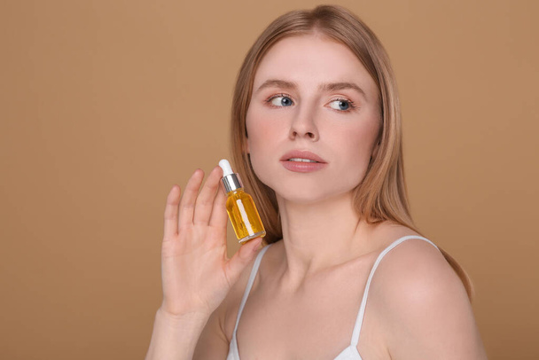 Beautiful young woman with bottle of essential oil on brown background - Foto, imagen