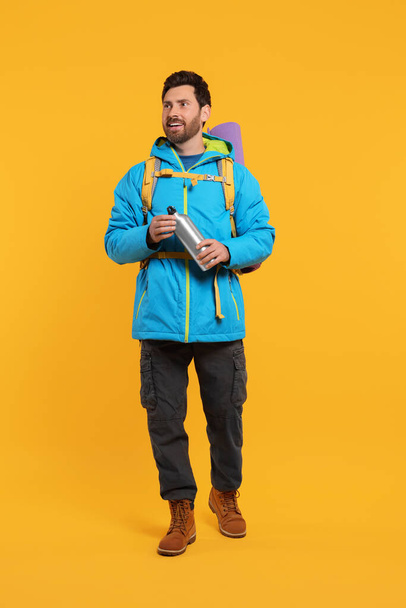Happy man with backpack and thermo bottle on orange background. Active tourism - Zdjęcie, obraz