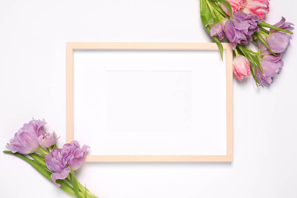 Empty photo frame and beautiful tulip flowers on white background, flat lay. Mockup for design - Photo, image