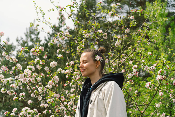 Красива молода жінка з весняними квітами насолоджується природою і сміється над весняним садом. Жінка тримає гілку яблуні. Концепція свободи та щастя. Весняний час
. - Фото, зображення