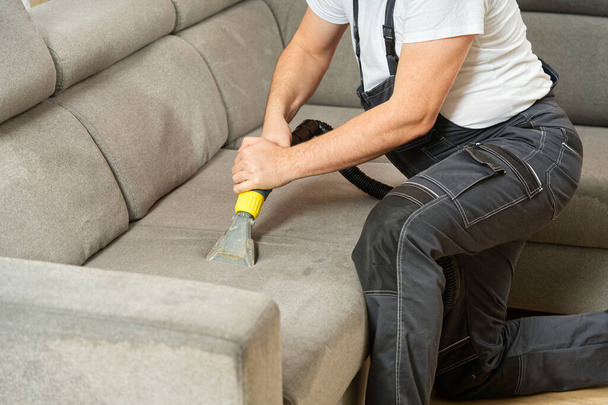 Dry cleaners man employee removing dirt from furniture in flat, closeup, vacuum clean sofa with professional equipment. cleaning sofa with washing suction cleaner closeup. - Foto, imagen
