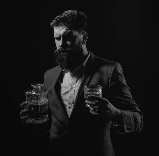 Bartender leather apron holding whisky cocktail in glass. Hipster with beard and mustache in suit drinks alcohol after working day - Foto, imagen