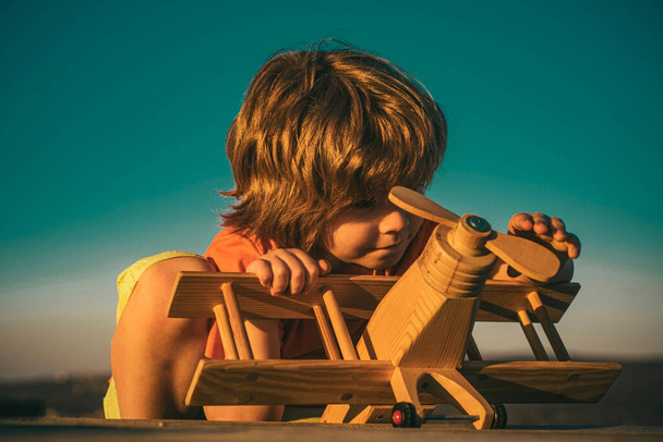 Child pilot with toy airplane dreams of traveling in summer in nature. Kids dreams. Child plays with a toy plane and dreams of becoming a pilot. Cute kids face - 写真・画像