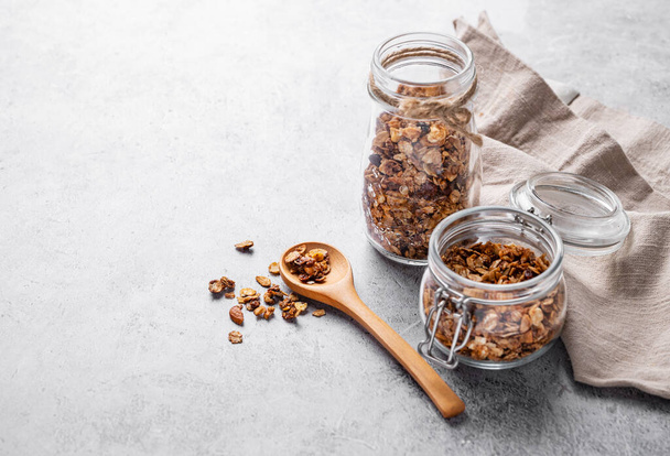 Homemade baked granola with nuts and raisins in a jar on a light background. Healthy vegetarian muesli for breakfast. Free space for text. - Zdjęcie, obraz