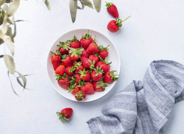 Juicy strawberries in a white bowl on a light blue background with napkin. Farm ripe healthy berries. Top view and copy space. - Photo, Image