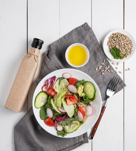 Вкусный овощной салат с помидорами, огурцом и редиской в тарелке на белом деревянном фоне с оливковым маслом. Концепция здорового питания. Вид сверху. - Фото, изображение