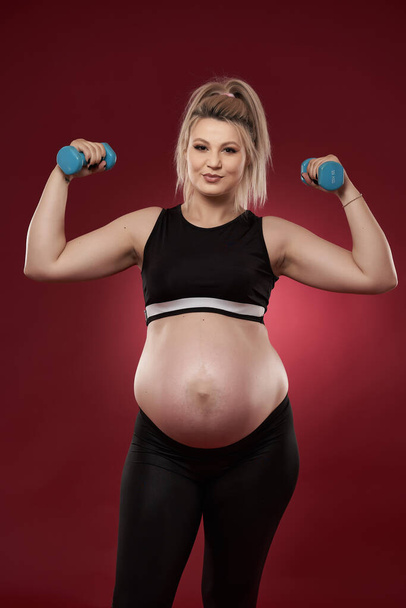 Young pregnant woman doing fitness exercises on red background, studio shot  - Фото, изображение