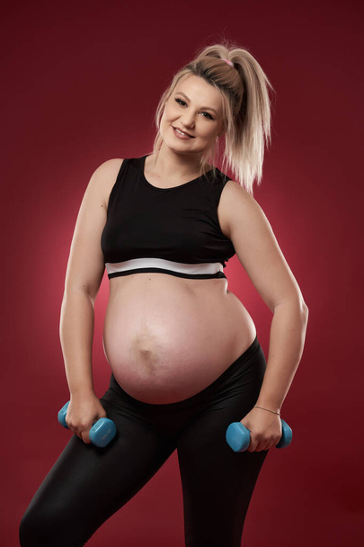 Young pregnant woman doing fitness exercises on red background, studio shot  - Foto, Bild