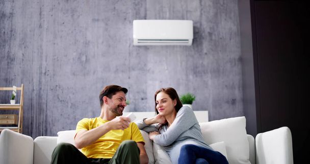 Happy Young Couple Adjusting Temperature Of Air Conditioner By Remote - Foto, Imagen