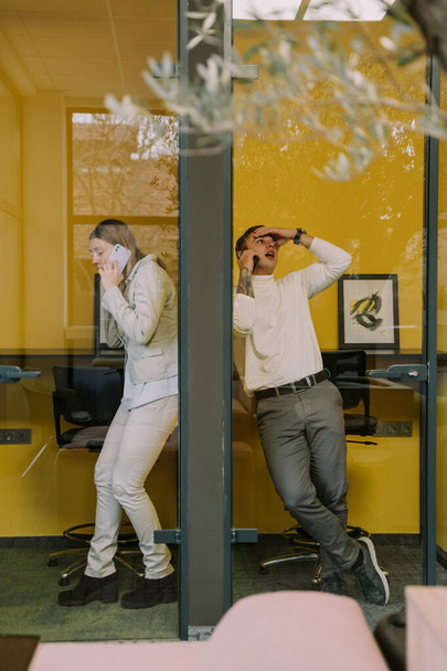Δύο ελκυστικοί άνδρες και γυναίκες συνάδελφοι που έχουν ένα τηλεφώνημα στους τηλεφωνικούς θαλάμους στο γραφείο - Φωτογραφία, εικόνα