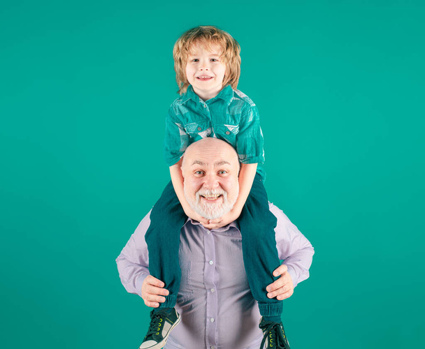 Grandfather and grandson piggyback ride with funny face isolated on blue in studio - Фото, изображение