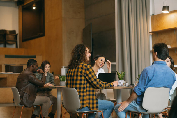 Выстрел молодой команды бизнесменов, которые весело общаются и улыбаются, работая вместе в современном кооперативном пространстве - Фото, изображение