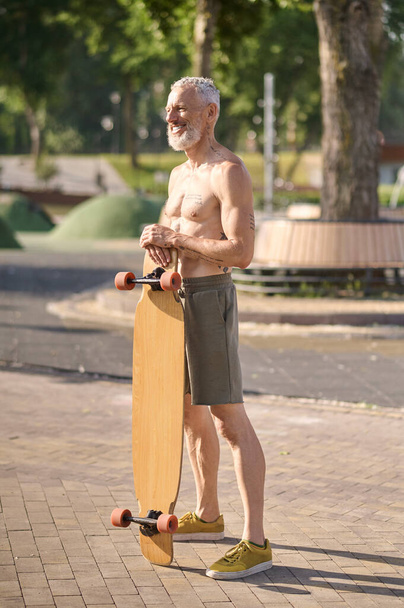 Smiling mature man holding longboard in a city park, active healthy lifestyle. - Fotoğraf, Görsel
