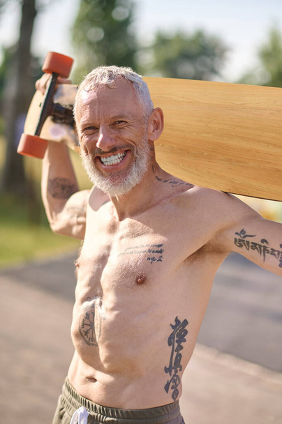 Lächelnder älterer Mann mit Longboard im Stadtpark, aktiver gesunder Lebensstil. - Foto, Bild