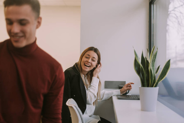 Όμορφη επιχειρηματίας γελάει με το συνάδελφό της, ενώ κάθεται στο co χώρο εργασίας - Φωτογραφία, εικόνα