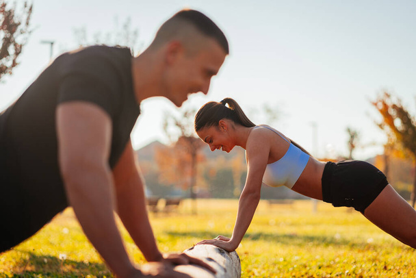 Beautiful couple having a fun conversation while doing push ups in the park, on a sunny day - Photo, Image