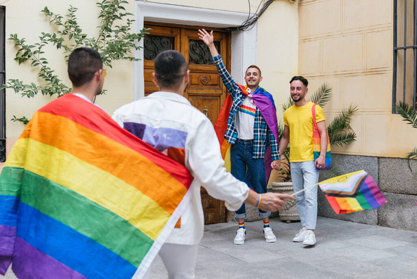 Дві пари геїв, переповнені радістю, вітаються біля входу в свій будинок з колекцією предметів гордості ЛГБТ.. - Фото, зображення
