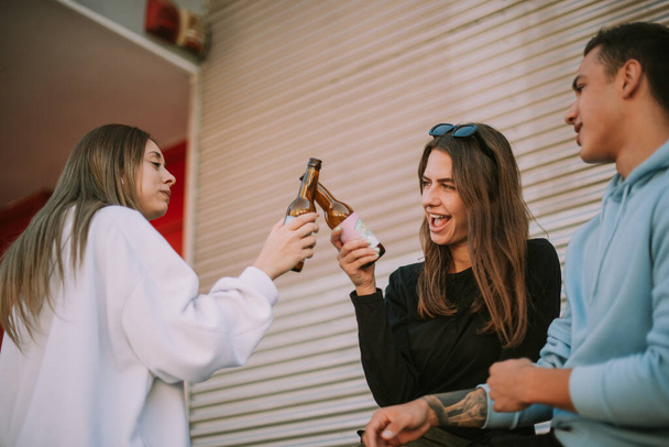 Close up of off two pretty girls making cheers with beer while standing with their firend - Foto, Imagem